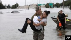 Petugas SWAT dari kepolisian Houston Daryl Hudeck menggendong Catherine Pam dan anaknya yang berumur 13 bulan, Aiden setelah menyelamatkan mereka dari rumah mereka yang dikepung banjir dari Badai Tropis Harvey, 27 Agustus 2017 di Houston. 