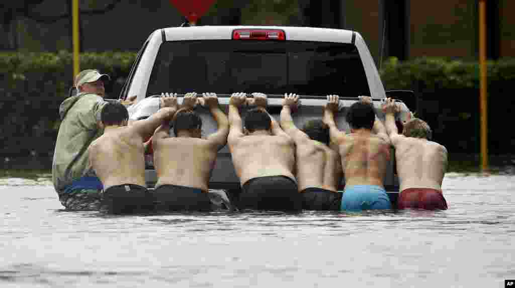People push a stalled pickup through a flooded street in Houston, after Tropical Storm Harvey dumped heavy rains, Sunday, Aug. 27, 2017. The remnants of Harvey sent devastating floods pouring into Houston on Sunday as rising water chased thousands of people to rooftops or higher ground. (AP Photo/Charlie Riedel)