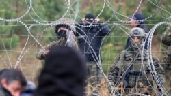 Polish border guards stand near the barbed wire as migrants from the Middle East and elsewhere gather at the Belarus-Poland border near Grodno, Belarus, Monday, Nov. 8, 2021. Poland increased security at its border with Belarus, on the European Union's eastern border, after a lar
