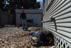 FILE - Shane Morning, 32, checks the pipes under his house for leaks while neighbor Walker Knott, 55, looks on, after an unprecedented winter storm in Houston, Texas, Feb. 19, 2021.
