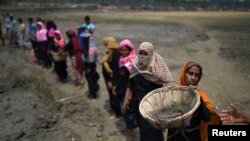 FILE - Rohingya refugee women carry baskets of dried out mud from the riverbed to help raise the ground level of their camp in preparation for monsoon season, in Shamlapur refugee camp, in Cox's Bazaar, Bangladesh, March 24, 2018.