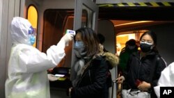Health Officials in hazmat suits check body temperatures of passengers arriving from the city of Wuhan at the airport in Beijing, China, Jan. 22, 2020.