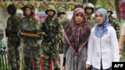 资料照：在新疆乌鲁木齐市的两名维吾尔族妇女步行经过中国武警队伍。 