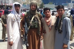 A Taliban fighter, second left, is seen with locals at Pul-e-Khumri on Aug. 11, 2021, after Taliban captured Pul-e-Khumri, the capital of Baghlan province.