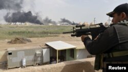 FILE - A member from the Iraqi security forces guards as smoke rises from Baiji oil refinery, north of Baghdad, Iraq May 26, 2015.