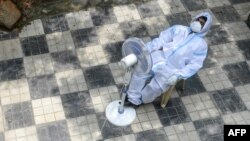 A health worker wearing a Personal Protective Equipment (PPE) suit takes a break sitting in front of a fan while waiting for to collect swab samples from residents for Covid-19 coronavirus tests at a public health centre in Hyderabad on September 17, 2020