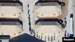 Anak-anak imigran, banyak di antaranya yang telah dipisahkan dari orang tuanya di bawah kebijakan baru “tanpa toleransi” pemerintahan Trump, tampak berjalan dalam satu barisan di antara tenda-tenda di komplek dekat perbatasan Meksiko di Tornillor, Texas, AS, 18 Juni 2018 (foto: REUTERS/Mike Blake)