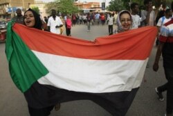 FILE - Sudanese women display their national flag in Khartoum, June 30, 2019.