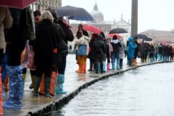 People walk on a catwalk in the flooded St. Mark's Square during a period of seasonal high water in Venice, Italy, Nov. 12, 2019.