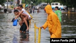 A Filipino man carries a girl as they negotiate a flooded street after a heavy downpour in suburban Quezon city, north of Manila, Philippines on Wednesday, June 17, 2015. AP Photo/Aaron Favila)