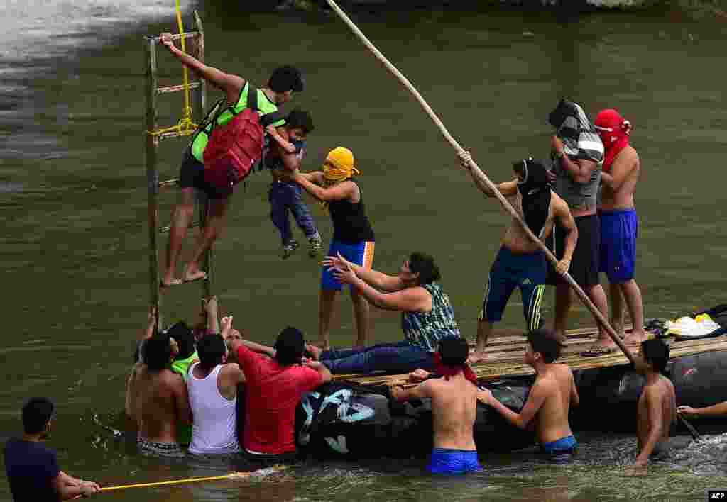 Honduran migrants heading in a caravan to the U.S., help a man holding a child get down to the Suchiate River from the Guatemala-Mexico international border bridge, in Ciudad Hidalgo, Chiapas state, Mexico, Oct. 20, 2018.