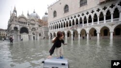 A tourist pushes her floating luggage in a flooded St. Mark's Square, in Venice, Italy, Nov. 13, 2019. 