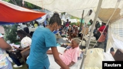 A woman is attended to by a member of the medical personnel outside a hospital after Saturday's 7.2 magnitude quake, in Les Cayes, Haiti, August 16, 2021.