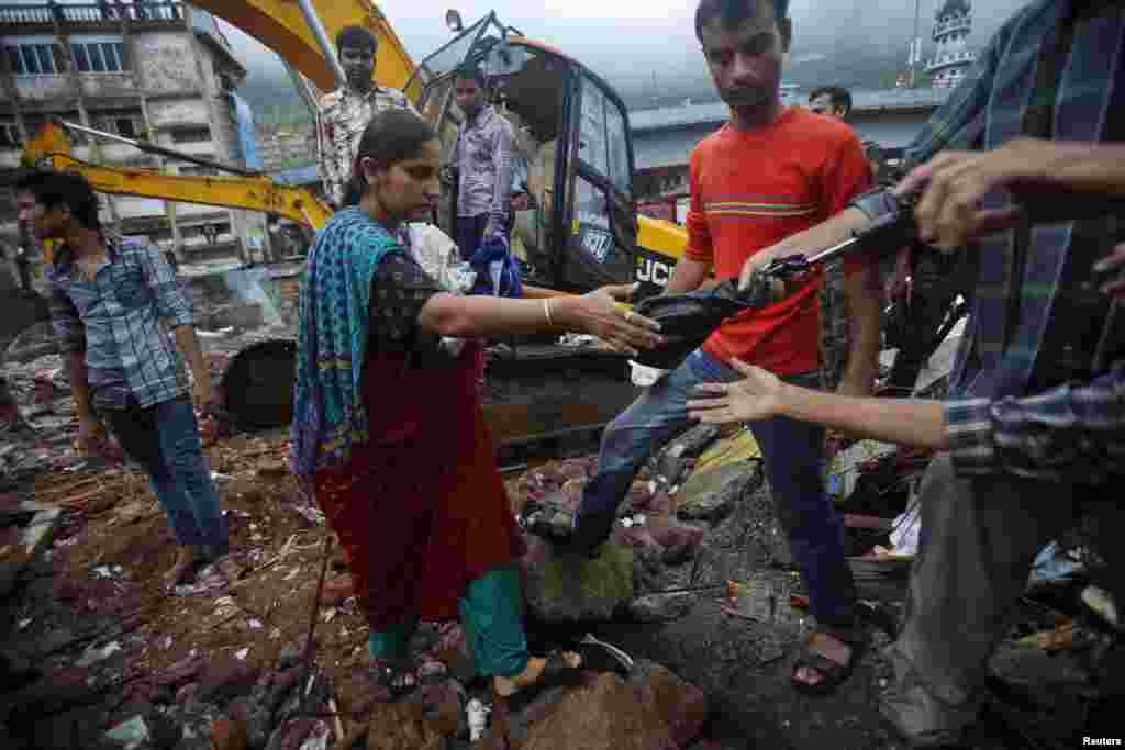 A resident receives help while carrying her possessions recovered from the rubble of a collapsed residential building on the outskirts of Mumbai, India, June 21, 2013. 