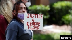 Seorang pemrotes memegang kertas di luar rumah Florida mantan Perwira Polisi Minneapolis Derek Chauvin, yang telah didakwa atas kematian George Floyd, di Windermere, Orlando, Florida, 29 Mei 2020. (Foto: Reuters)