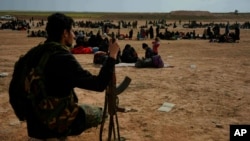 FILE - A member of U.S.-backed Syrian Democratic Forces watches over people who were evacuated out of the last territory held by Islamic State militants, outside Baghouz, Syria, March 5, 2019.