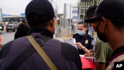 FILE - A US Customs and Border Protection officer examines paperwork of migrants waiting to cross into the United States to begin the asylum process, July 5, 2021, in Tijuana, Mexico.