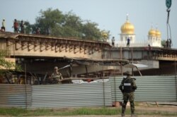 FILE - A Pakistani soldier, right, and an Indian soldier stand between steel sheets beside a bridge being built to lead to the Sikh religious site Gurdwara Darbar Sahib, in the Pakistani town of Kartarpur, near the Indian border, Sept. 16, 2019.