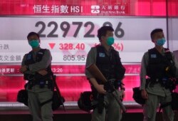 Riot police wearing face masks stand guard in front of a bank electronic board showing the Hong Kong share index at Hong Kong Stock Exchange, May 28, 2020.