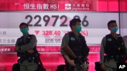 Riot police wearing face masks stand guard in front of a bank electronic board showing the Hong Kong share index at Hong Kong Stock Exchange, May 28, 2020.