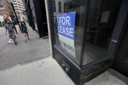 Passers-by wear masks to protect against the coronavirus as they walk past an empty business location, in Boston's Downtown Crossing neighborhood, Aug. 2, 2020.
