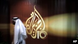 Seorang karyawan jaringan televisi Al-Jazeera berjalan melewati logo yang terpasang di pusat kantor stasiun berita tersebut di Doha, Qatar (Foto: dok).