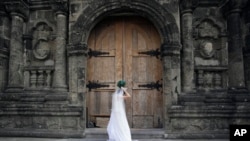 FILE - On her wedding day, a Filipino bride fixes her gown before entering a Catholic church in Manila, Philippines. (AP Photo/Aaron Favila)