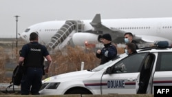 TOPSHOT - French customs officers stand next to a customs car with an Airbus A340 in the background which was grounded on the tarmac since Dec. 21 over suspected "human trafficking", at the Vatry airport, north-eastern France on Dec. 25, 2023.