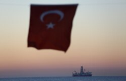 FILE - The Turkish national flag hangs in the foreground as drilling vessel Fatih is seen off the Mediterranean resort city of Antalya, Turkey