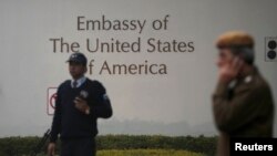 A U.S. embassy security guard (L) and an Indian policeman stand in front of the main gate of the embassy as the bulldozer (unseen) removes the security barriers, in New Delhi Dec. 17, 2013. 