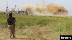 FILE - An Islamist rebel fighter walks by as smoke rises after what activists said was an airstrike by forces of Syria's President Bashar al-Assad at Qarmeed camp, after Islamist rebel fighters took control of the area, April 2015. 