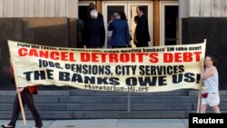 Protesters carry a banner calling for Detroit's debt to be cancelled as people enter the federal courthouse for day one of Detroit's municipal bankruptcy hearings in Detroit, Michigan July 24, 2013. 