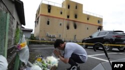 A man prays next to flowers and tributes laid at the scene where over 30 people died in a fire at an animation company building in Kyoto, Japan, on July 19, 2019. A suspected arson attack at an animation production company in Japan killed 33 people and in