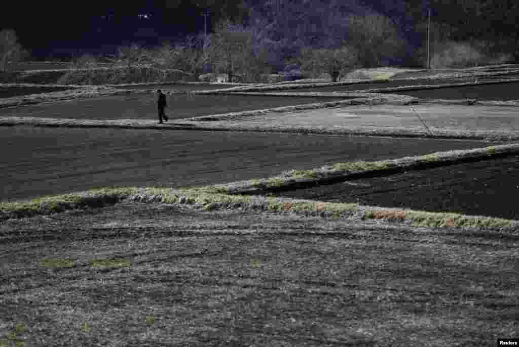 Seorang pria berjalan di antara sawah-sawah yang tidak ditanami di Miyakoji, Tamura di prefektur Fukushima (1/4).