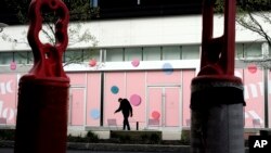 FILE - A passer-by walks past pedestrian traffic pylons in an outdoor mall where most stores remain closed out of concern for the coronavirus, in Dedham, Mass., April 22, 2020.