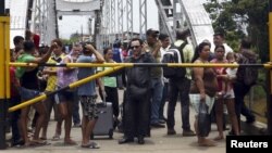 FILE - People stand next to a closed gate as they wait to try to cross La Union international bridge, on the border with Colombia at Boca de Grita in Tachira state, Venezuela, Aug. 29, 2015. 