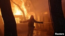 FILE - A firefighter reacts as a wildfire burns at Varympompi suburb north of Athens, Greece, August 3, 2021. 