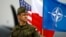 FILE - A Polish soldier stands in front of U.S., Polish and NATO flags ahead of military exercises in Swidwin, northwestern Poland, April 23, 2014.