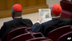 Spanish Cardinal Ricardo Blazquez Perez, right, reads a newspaper showing a picture of gay bishop Krzysztof Charamsa and his partner Eduard before the start of the morning session of the Synod of bishops on family issues, at the Vatican, Friday, Oct…