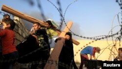 Warga yang baru mengungsi membawa paket bantuan kemanusiaan setelah mereka melompati dinding, sementara asap kebakaran mengepul dari kilang minyak di Qayyara, selatan Mosul, Irak, 25 Oktober 2016. (Foto: REUTERS/Zohra Bensemra)