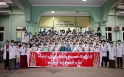 FILE: Medical staff hold up a three-finger salute and a banner that reads they "oppose the military coup against the people" during a protest against the military takeover, at a hospital in Naypyidaw on February 5, 2021. (Photo by STR / AFP)