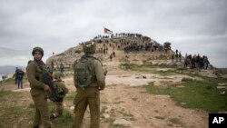 FILE - Israeli soldiers take position as Palestinian demonstrators gather during a protest against expansion of Israeli settlements, in the West Bank village of Beita near Nablus, March 2, 2020.