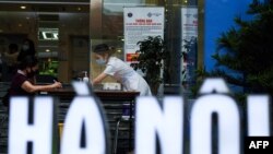 FILE - A health worker (R) assists a woman filling up a health declaration form outside the Hanoi General Hospital before entering the medical facility in Hanoi on May 5, 2021. 