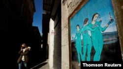 FILE - A woman wearing a protective face mask walks past a painting representing Moderna, Pfizer and AstraZeneca vaccines at Bisbe street, during the COVID-19 outbreak, in Barcelona, Spain, Jan. 27, 2021.