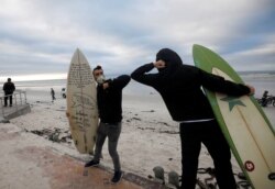 FILE - Surfers bump elbows as they protest against the nationwide lockdown regulations that allow exercise but not water activities, amid the coronavirus disease (COVID-19) outbreak, at Muizenberg beach in Cape Town, South Africa, May 5, 2020.