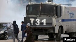People walk past an armored police vehicle as Turkish riot police use tear gas to disperse Kurdish demonstrators during a protest against a curfew in Sur district and security operations in the region, in the southeastern city of Diyarbakir, Turkey, Jan. 
