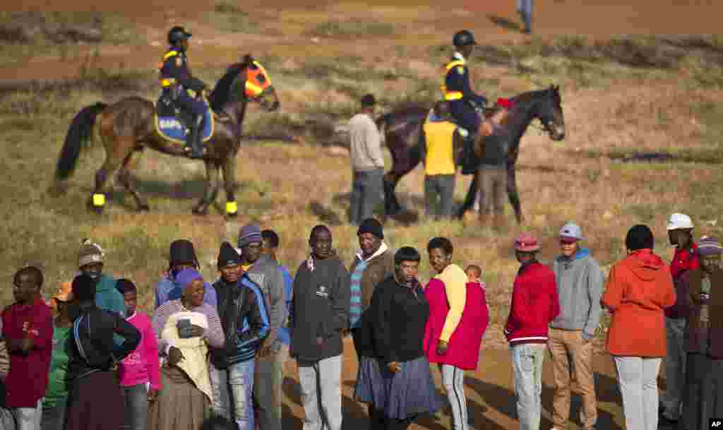 Para warga Afrika Selatan mengantre untuk memberikan suaranya saat polisi memberi pengamanan ketat dekat sebuah TPS yang dibakar malam sebelumnya. Sebuah tenda didirikan untuk menggantikan TPS di kota pertambangan yang rentan konflik politik di Bekkersdal, Afrika Selatan (7/5). (AP/Ben Curtis)
