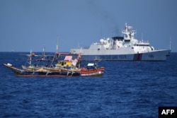 Sebuah kapal penjaga pantai China (latar belakang kanan) berlayar melewati kapal nelayan Filipina di dekat Scarborough Shoal yang dikuasai China, di Laut China Selatan. (Foto: AFP)