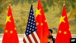 FILE - Chinese staffers adjust U.S. and Chinese flags before a session of negotiations between U.S. and Chinese trade representatives, at the Diaoyutai State Guesthouse, in Beijing, China, Feb. 14, 2019.