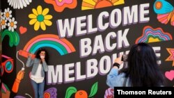 People take photos in front of a 'Welcome Back' sign after coronavirus disease restrictions were eased in Melbourne, Nov. 4, 2020.